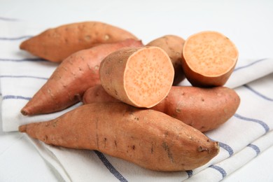 Whole and cut ripe sweet potatoes on kitchen towel, closeup