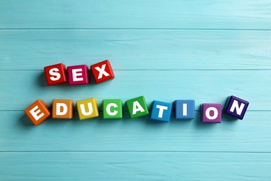 Colorful wooden blocks with phrase "SEX EDUCATION" on light blue background, flat lay
