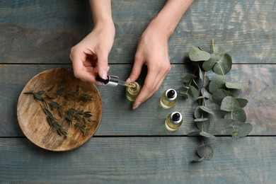 Woman taking eucalyptus essential oil with dropper from bottle at wooden table, top view