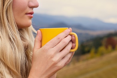 Young woman with mug of hot drink in mountains, closeup. Space for text