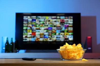 Bowl of chips and TV remote control on table indoors. Space for text