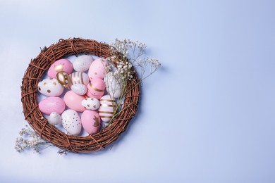 Photo of Festively decorated Easter eggs, vine wreath and gypsophila flowers on light blue background, top view. Space for text