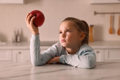 Cute little girl refusing to eat apple in kitchen