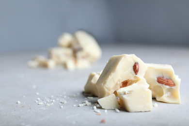 Photo of Pieces of white chocolate with nuts on light grey table. Space for text