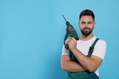 Young worker in uniform with power drill on light blue background. Space for text