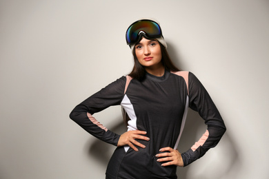 Woman wearing thermal underwear and goggles on light grey background. Winter sport clothes