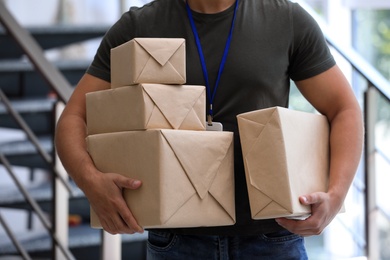 Young courier with parcels indoors, closeup. Delivery service