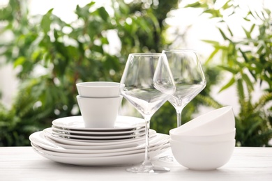 Set of clean dishware and wineglasses on white table against blurred background