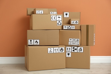 Cardboard boxes with different packaging symbols on floor near orange wall. Parcel delivery