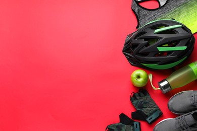 Flat lay composition with different cycling accessories and clothes on red background, space for text