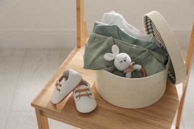 Box with baby bodysuits, booties and toy on chair indoors