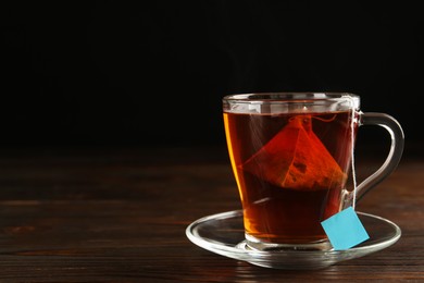 Photo of Tea bag in glass cup of hot water on wooden table. Space for text