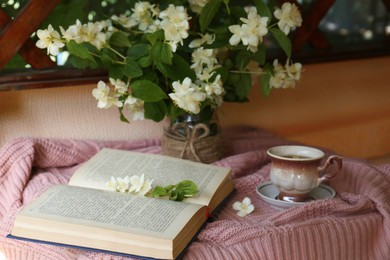 Beautiful jasmine flowers, cup of aromatic drink and open book on pink fabric indoors
