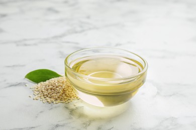 Glass bowl of sesame oil and seeds on white marble table