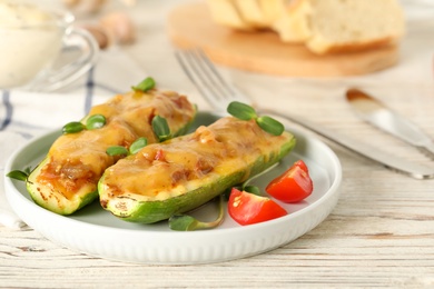 Baked stuffed zucchinis served with tomatoes on white wooden table, closeup