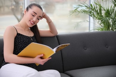 Photo of Happy woman reading magazine on sofa at home