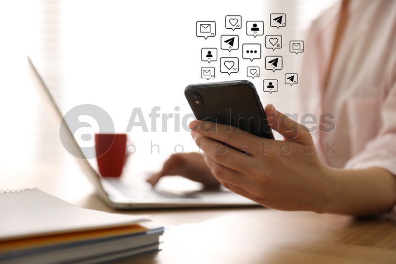 Different virtual icons and young woman using smartphone and laptop at table indoors, closeup. SMM (Social media marketing) concept
