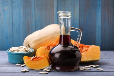 Fresh pumpkin seed oil in glass jug on grey wooden table