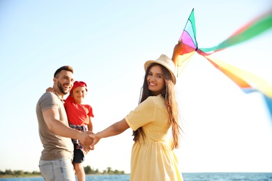 Happy parents and their child playing with kite near sea. Spending time in nature