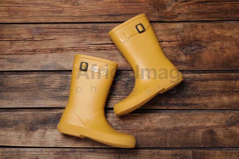 Pair of yellow rubber boots on wooden background, top view