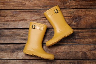 Pair of yellow rubber boots on wooden background, top view