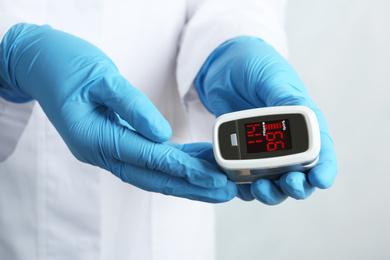 Doctor holding modern fingertip pulse oximeter, closeup