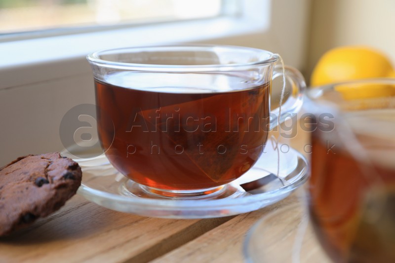 Bag of black tea in cups on wooden table indoors, closeup