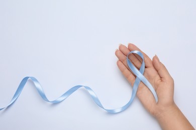 Woman holding light blue awareness ribbon on white background, top view