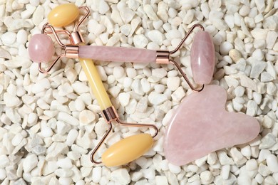 Quartz gua sha tool and face rollers on white stones, flat lay