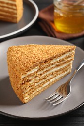 Photo of Slice of delicious layered honey cake served on black wooden table, closeup