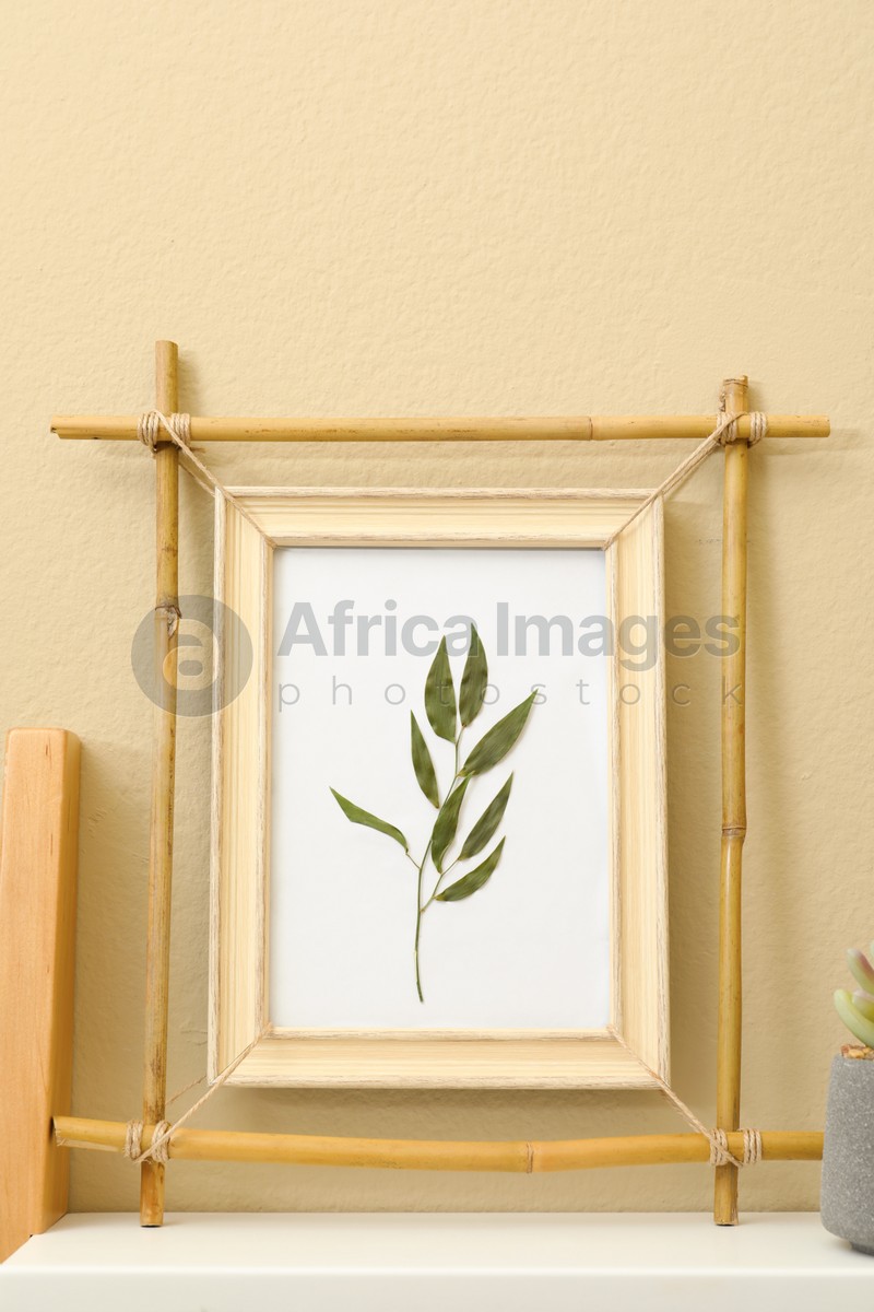 Bamboo frame with floral picture on shelf near beige wall