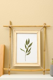 Bamboo frame with floral picture on shelf near beige wall