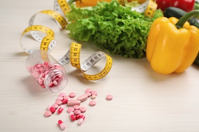 Weight loss pills, different vegetables and measuring tape on white wooden table