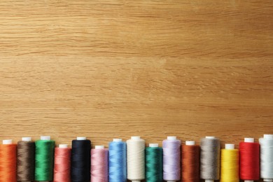Many colorful sewing threads on wooden table, flat lay. Space for text