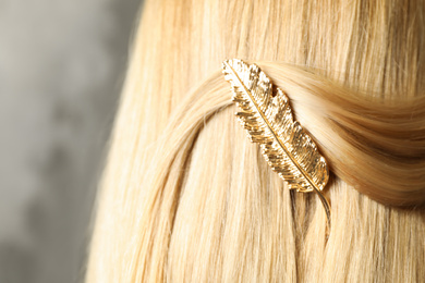 Woman with beautiful gold hair clip on grey background, closeup
