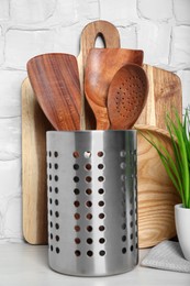Set of wooden kitchen utensils, board and houseplant on table near white wall