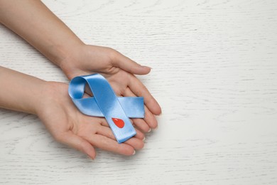 Woman holding light blue ribbon with paper blood drop at wooden table, top view and space for text. Diabetes awareness