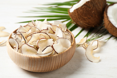 Tasty coconut chips on white wooden table