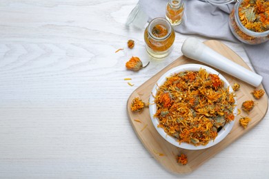 Dry calendula flowers and bottles with tincture on white wooden table, flat lay. Space for text