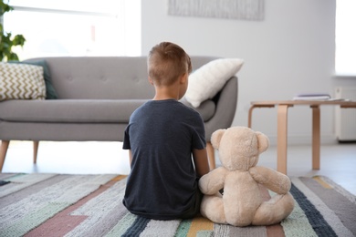 Lonely little boy with teddy bear sitting on floor at home. Autism concept