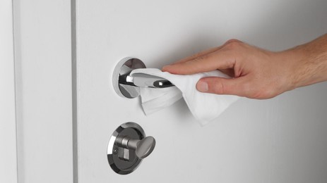 Man cleaning doorknob with disinfecting wipe indoors, closeup. Protective measures