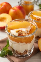 Tasty peach yogurt with granola, pieces of fruit and jam on table