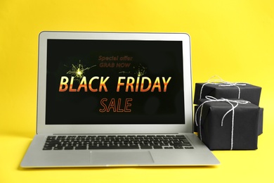 Laptop with Black Friday announcement and gifts on yellow background