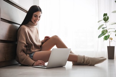 Woman with laptop sitting on warm floor at home. Heating system