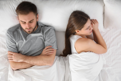 Upset young woman near sleeping husband in bed, top view. Relationship problems