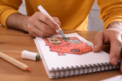 Man drawing in sketchbook with felt tip pen at wooden table, closeup
