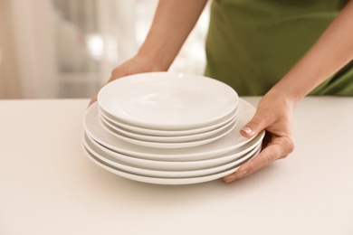 Woman putting stack of clean dishes on table indoors, closeup