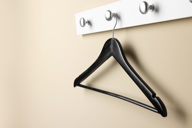 Rack with empty black clothes hanger on beige wall. Space for text