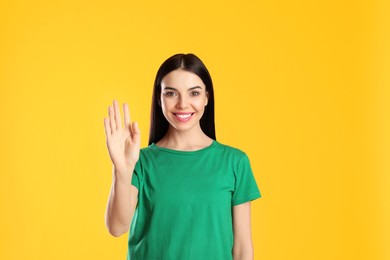 Attractive young woman showing hello gesture on yellow background