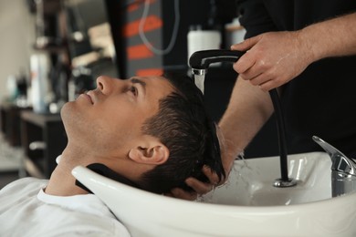 Professional barber washing client's hair at sink in salon, closeup